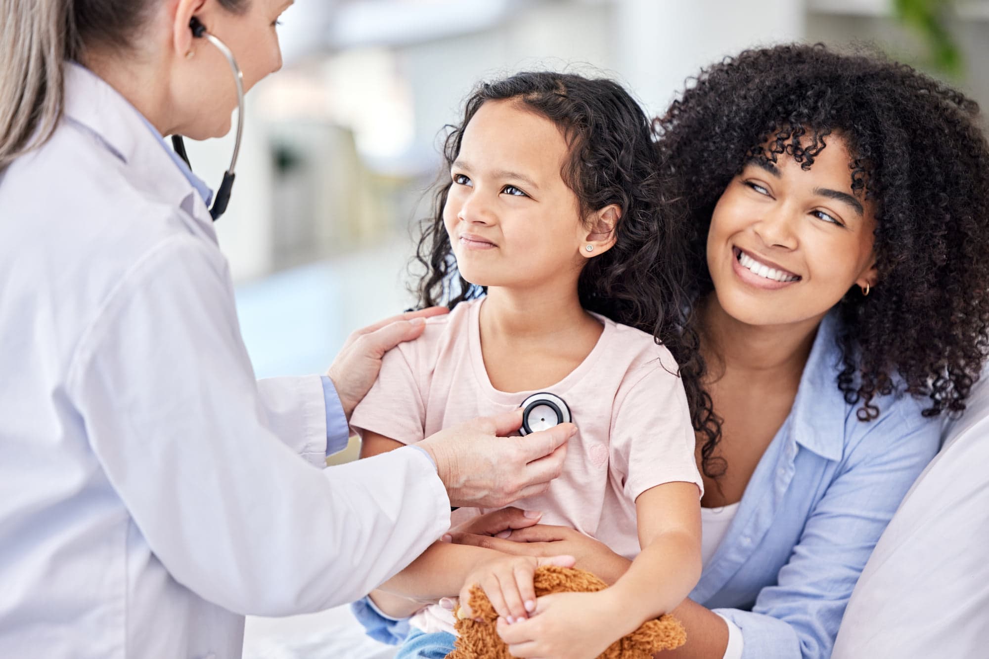 A girl on her mother's lap during a check-up, the provider listening to her heartbeat