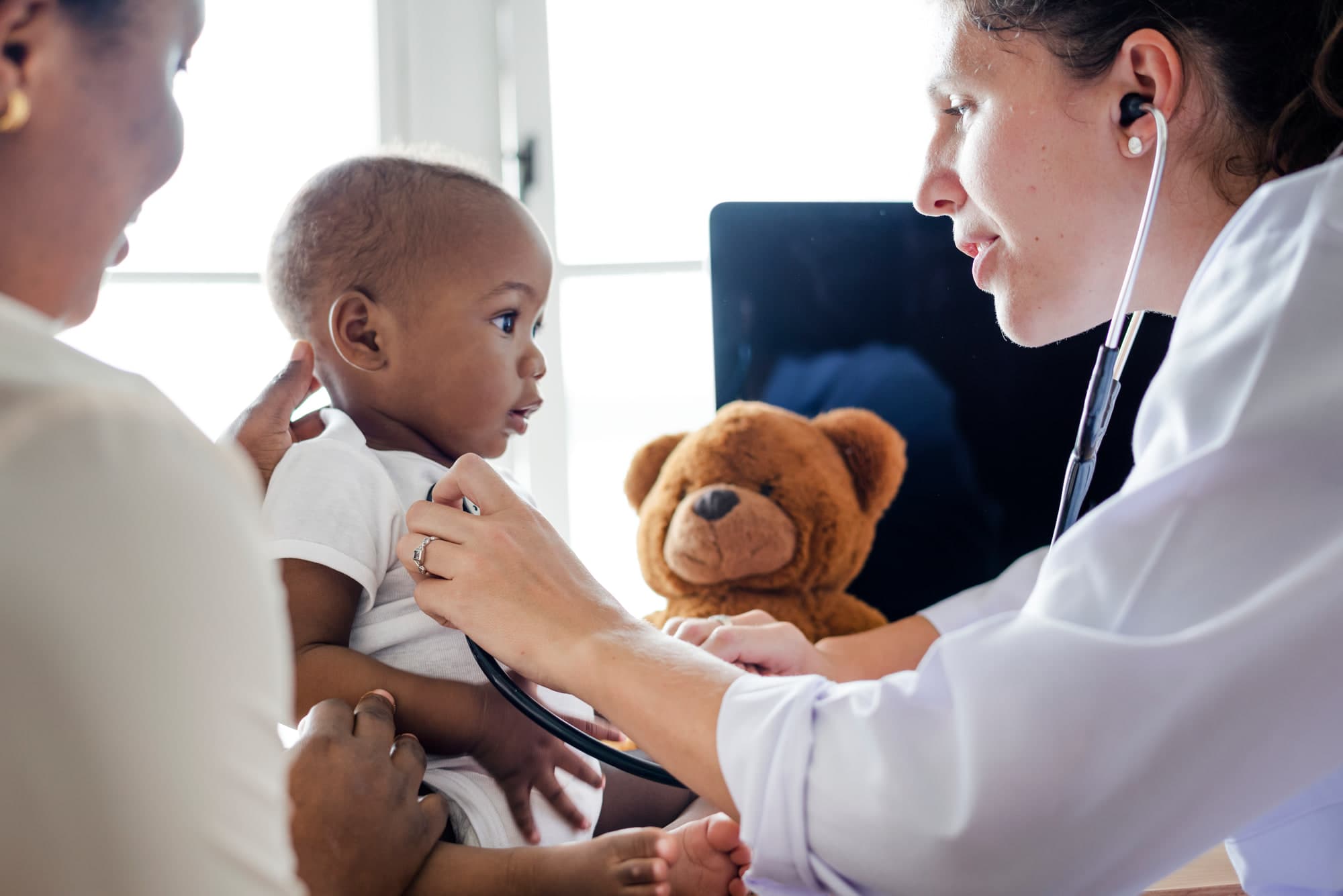 A pediatrician examining a baby held by a parent